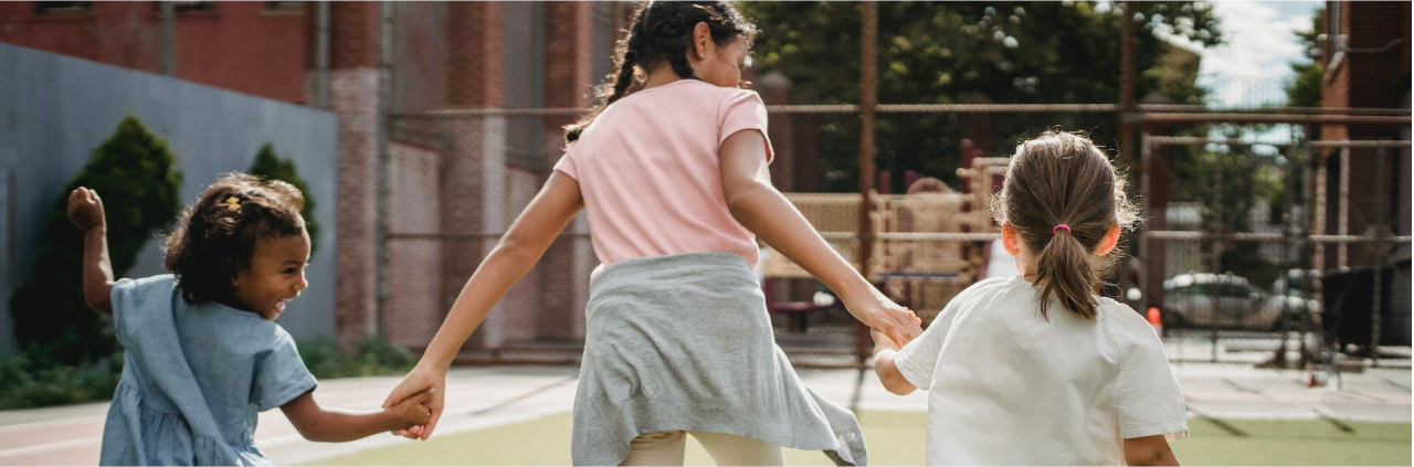Diverse group of children holding hands as they run together in a park.