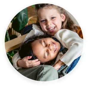 Two girls laughing together as one girl hugs the other on her lap.